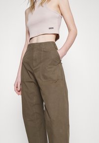 Ribbad, kort tanktop i ljusbeige som matchas med lösa, högmidjade byxor i olivgrön med stora sidofickor och en slät yta.