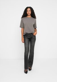 Grå kortermet t-skjorte med nagledetaljer ved halsen, kombinert med mørkegrå vide jeans og svarte spissede sko.