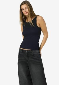 Top de tirantes negro acanalado con escote amplio, combinado con jeans de mezclilla negros holgados que tienen cinco bolsillos y un cierre de botón.