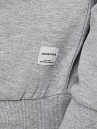 Felpa grigia in tessuto morbido, con orlo a costine, e un'etichetta con "JACK & JONES" e "AUTHENTIC JEANSWEAR SINCE 1990."