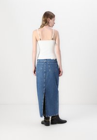 Blue denim maxi skirt with a high slit, paired with a white tank top. Features a classic five-pocket design and belt loops. Black ankle boots.