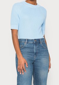 Jasnoniebieski prążkowany sweter z krótkim rękawem i okrągłym dekoltem, zestawiony z jasnoniebieskimi, wysokim stanem dżinsami. Gładka faktura, dopasowany krój.