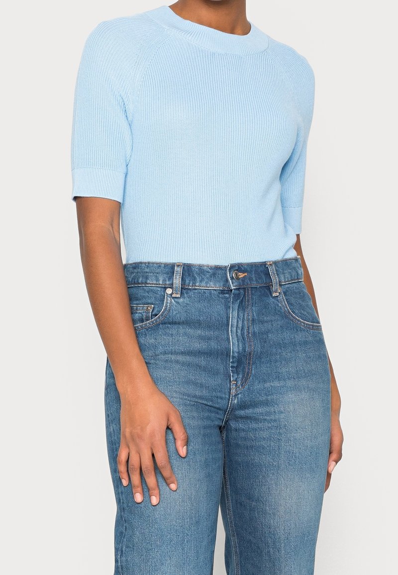 Jasnoniebieski prążkowany sweter z krótkim rękawem i okrągłym dekoltem, zestawiony z jasnoniebieskimi, wysokim stanem dżinsami. Gładka faktura, dopasowany krój.