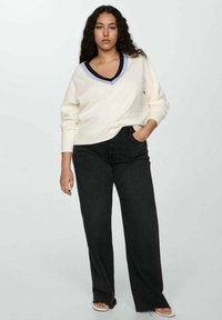 Krämsfärgad v-ringad tröja med en marinblå och ljusblå ribbad halsringning, ihop med högmidjade svarta vida jeans, bärs med vita sandaler med öppen tå.