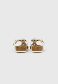 Bele sandale s ploskvico iz plute, nastavljivim trakom z zlato opremo, odprtim zadnjim delom, teksturirano podplatom za oprijem, minimalistična oblika.