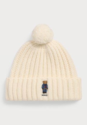 Caciula tricotată crem, cu un model texturat, având un pom-pom în vârf și un urs brodat îmbrăcat într-o ținută albastră, cu textul "Polo".