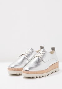Chaussures lacées métalliques argentées avec une surface texturée, semelle compensée semblable à du liège et bord cranté. Présente un laçage crème clair.