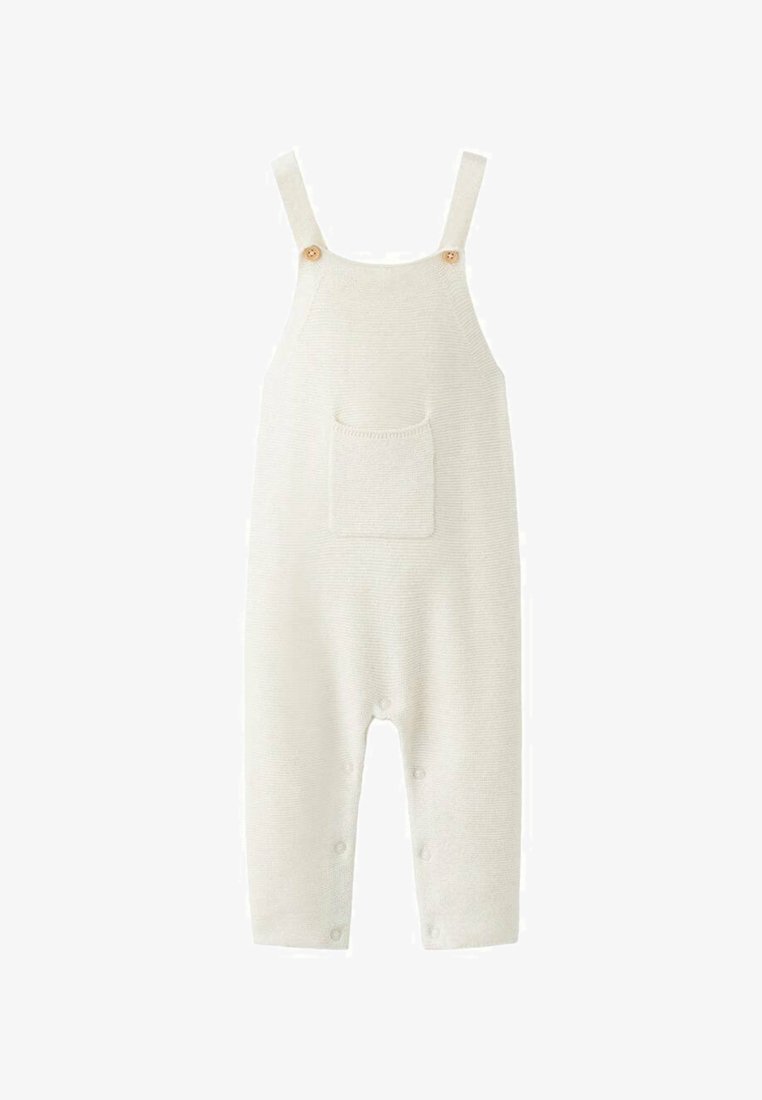 Combinaison beige tricotée avec bretelles larges, boutons en bois, une poche frontale et des fermetures à boutons aux jambes pour faciliter l'habillage.