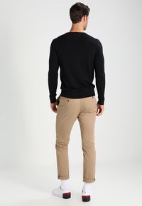 Schwarzer Langarmpullover kombiniert mit beigen Hosen. Die Hosen sind an den Säumen hochgekrempelt, und weiße Sneaker mit roten Akzenten runden das Outfit ab.