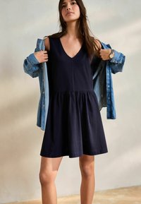 Robe sans manches bleu marine avec un décolleté en V, jupe froncée et veste en jean. Texture lisse, design décontracté, adaptée aux temps chauds.