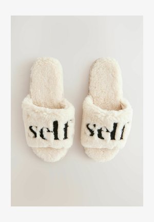Flauschige Cremeslipper mit einem samtigen Außenmaterial. Schwarzer "Selbst"-Text auf der Vorderseite. Offenes Design mit einer weichen, strukturierten Oberfläche.