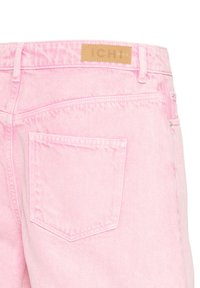 Gros plan d'un jean en denim rose vu de dos avec une unique poche arrière et une étiquette en cuir beige cousue à la ceinture.