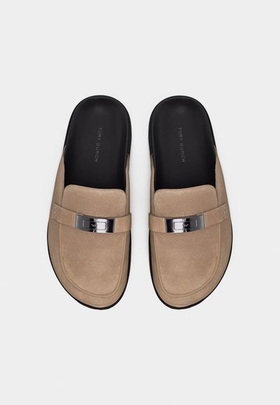 Μπεζ μοκασίνια από σουέντ χωρίς κορδόνια με μαύρα πέλματα, μεταλλική αγκράφα και στρογγυλεμένες τετράγωνες μύτες, φωτογραφημένα από πάνω.