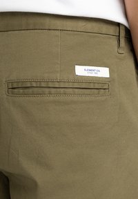 Olivgrüne Hosen aus robustem Stoff, mit einer Gesäßtasche und einem weißen Etikett mit blauer Schrift, auf dem "ELEMENT CO. SINCE 1992." steht.