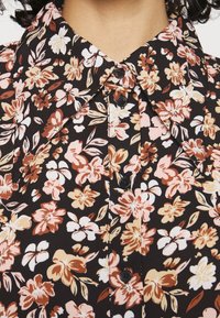Camicia nera a fiori con colletto, piccoli pulsanti e un mix di fiori rosa, bianchi e marroni su uno sfondo scuro.