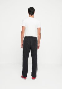 Black sweatpants with white side stripes, elastic waistband, and a back pocket, paired with a plain white t-shirt and red shoes.