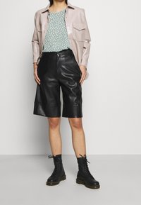 Camicia sintetica rosa chiaro, top a motivi verdi, pantaloni corti in pelle nera, stivali neri stringati con suole spesse. Tessuto liscio, vestibilità comoda.