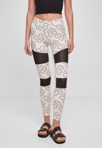 Blomstertrykte leggings i beige med sorte kanter, med gjennomsiktige sorte paneler på knærne, kombinert med svarte sandaler med stropper og platå.
