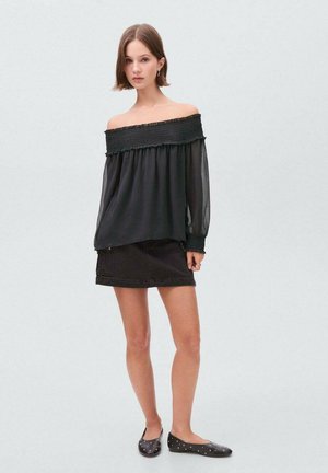 Schwarze schulterfreie Bluse mit gesmoktem Oberteil und transparenten langen Ärmeln, kombiniert mit einem schwarzen Jeans-Minirock und schwarzen Ballerinas mit Nieten.