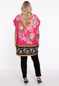 Roze tuniek met bloemenpatroon en een onderband in zwart, geel en roze. Met strik-mouwen en een losse pasvorm. Draag met zwarte broeken.