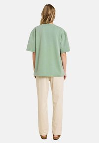 T-shirt oversized vert menthe à manches courtes associé à un pantalon beige clair, ample et décontracté. Le tissu semble doux et décontracté.