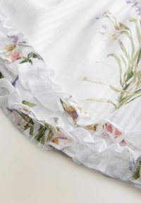 Hvidt stof med lodrette striber har en flæset kant prydet med blomster mønstre i pink, gul og grønnuancer.