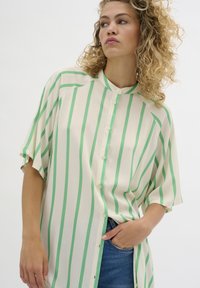 Bluză rayată verde și albă, cu mâneci scurte, închidere cu butoane în față, design fără guler, material moale, cu cusături vizibile și slituri pe laterale.