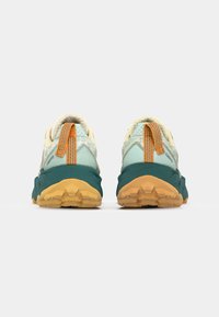 Des chaussures de trail avec un dessus vert clair et teal, des accents orange, un col rembourré et une semelle extérieure texturée jaune pour une bonne traction.