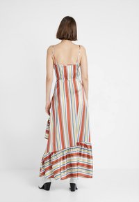 Maxi sukienka bez ramiączek i pleców w pionowe paski w kolorach czerwonym, pomarańczowym, żółtym i niebieskim, z falbaną u dołu i zwiewnym materiałem.