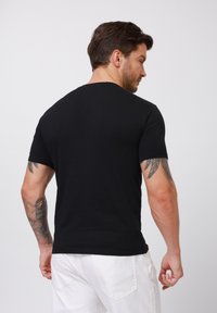 Black cotton t-shirt with short sleeves and a crew neck, featuring a smooth texture and a plain design, viewed from the back.