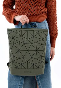 Bolsa tote verde oliva con un patrón geométrico negro, fabricada con un material liso, que cuenta con asas cortas y un logo en la base.