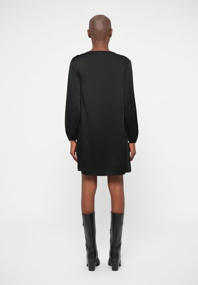 Rochie din satin neagră cu mâneci lungi bufante, decolteu rotund și siluetă dreaptă, asortată cu cizme negre cu toc înalt.