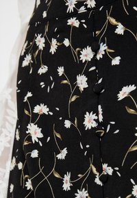 Musta kangas, jossa on kukkakuosi, joka sisältää valkoisia päivänkakkaroita ja kultaisia yksityiskohtia. Sivusaumaa koristavat kuusi nappia. Sileä pinta.