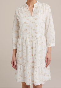 Vit klänning med långa ärmar, beige blommig brodyr, V-ringning och en veckad, fållad kjol. Mjukt, lätt tyg.