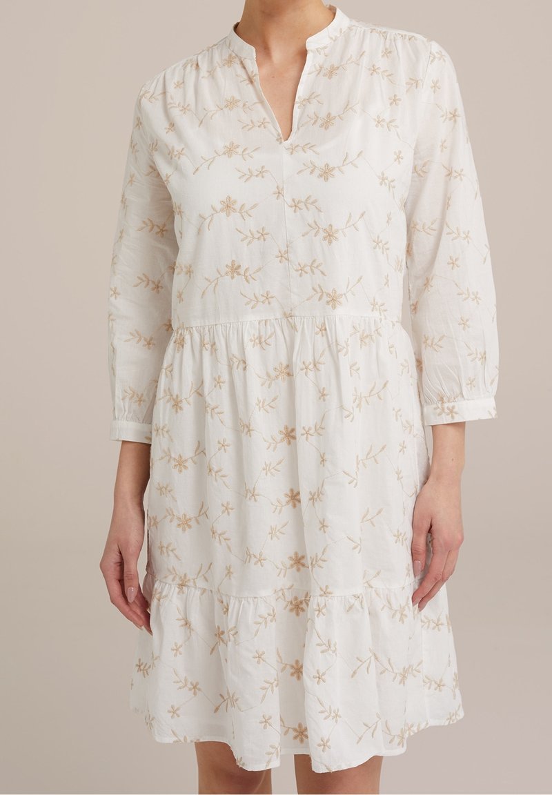 Vit klänning med långa ärmar, beige blommig brodyr, V-ringning och en veckad, fållad kjol. Mjukt, lätt tyg.