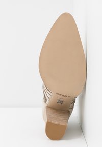 Chaussure à talon haut beige avec bout pointu, semelle marron clair texturée et accents argentés. Présente des rayures verticales sur le dessus.