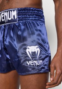 Tengerészkék szatén bokszrövidnadrág rugalmas derékpánttal, fehér "VENUM" logóval és kígyó grafikával, oldalsó hasításokkal a mozgékonyságért, sima textúrával.