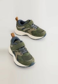 Para zielono-beżowych dziecięcych sneakersów z siateczkowej tkaniny, z rzepami, sznurówkami i brązowymi pętlami do ciągnięcia na białym tle.