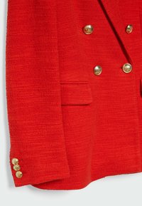 Blazer rouge texturé avec des boutons dorés à double boutonnage et une poche avant unique. Il présente une coupe cintrée et des accents de boutons contrastants sur les manches.