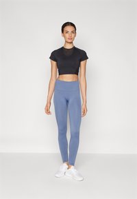 Čierny športový top s krátkymi rukávmi, skrátený, v kombinácii so svetlomodrými legínami s vysokým pásom a bielymi športovými topánkami. Hladká textúra látky.