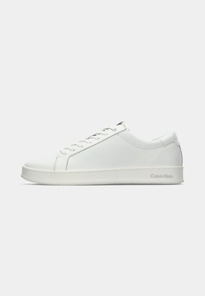 Lage witte leren sneaker met witte veters en dikke zool, Calvin Klein-logo gedrukt aan de zijkant nabij de hiel.