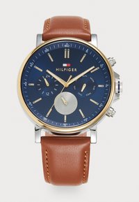 Montre avec un bracelet en cuir marron, un cadran bleu, des accents dorés et un boîtier en argent. Les caractéristiques incluent des sous-cadrans pour le jour, la date et le format 24 heures.