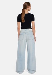 Top corto a maniche corte nero a costine abbinato a jeans a gamba larga azzurri chiari, con vita alta e tasche posteriori, visto da dietro.