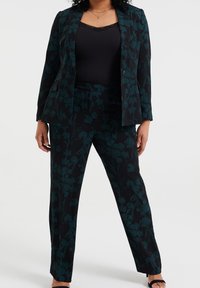 Svart kostym med blommönster, inklusive en figursydd kavaj och raka byxor, med mörkgröna detaljer och en mjuk tygtextur.