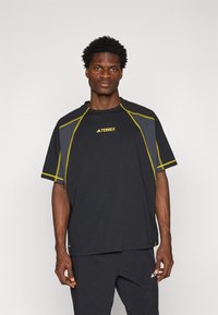 T-shirt atlético preto com costuras amarelas, mangas curtas, gola redonda e logótipo "TERREX" no peito. Feito de material respirável.