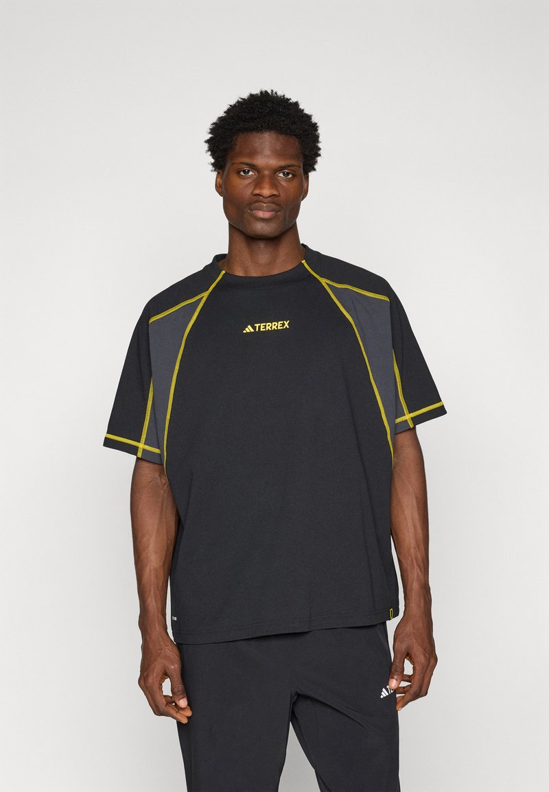 T-shirt atlético preto com costuras amarelas, mangas curtas, gola redonda e logótipo "TERREX" no peito. Feito de material respirável.