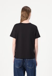 Svart kortermet t-skjorte, bomullstoff, avslappet passform, rund halslinning, brukt med blå høyt belte jeans, ensfarget uten mønstre eller detaljer.