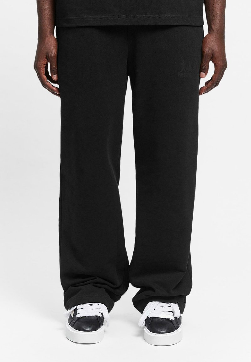 Black cotton sweatpants with a relaxed fit, featuring a subtle logo detail and paired with black and white sneakers.