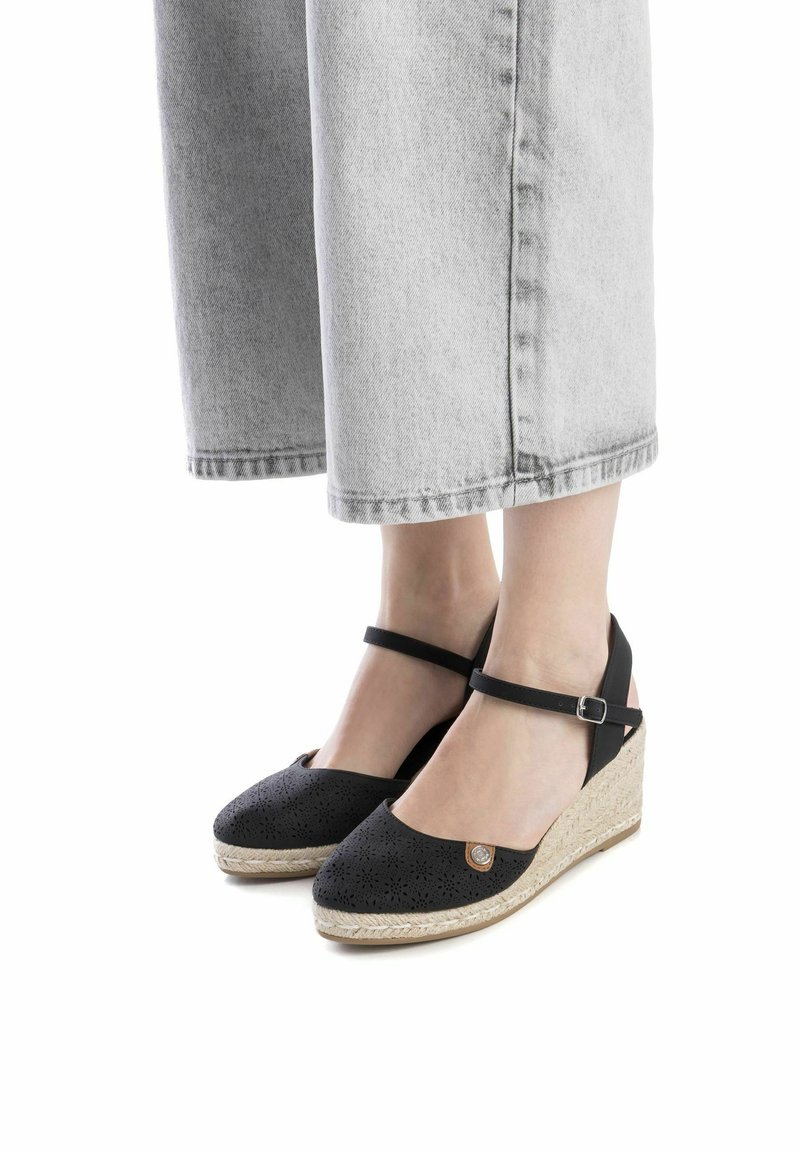 Espadrilles noires à talon compensé avec un dessus perforé, une sangle de cheville et une semelle intermédiaire en jute tressé. Présente un accent décoratif en forme de logo rond.