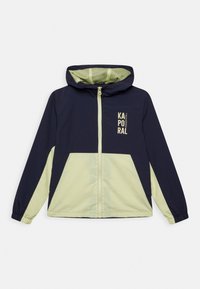 Granatowo-zielona kurtka z kapturem, zapinana na zamek, z elastycznymi mankietami, z nadrukowanym logo w górnej lewej części. Gładka tkanina, lekka konstrukcja.